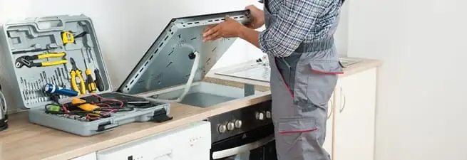 Cooktop repair technician lifting a built-in stovetop for service in Colorado Springs, CO
