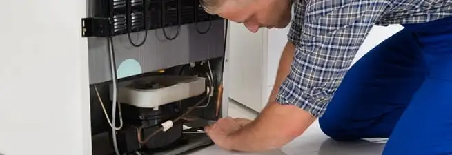 Refrigerator repair technician servicing the compressor and condenser area in Colorado Springs, CO