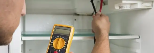 Refrigerator repair technician testing electrical components with a multimeter in Colorado Springs, CO