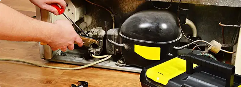 Refrigerator repair technician fixing the compressor and wiring in Colorado Springs, CO